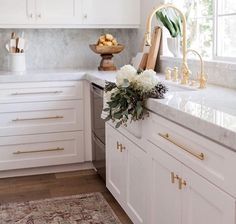 a kitchen with white cabinets and marble counter tops, gold accents on the faucet