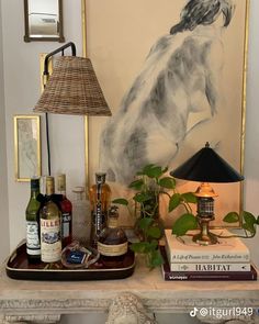 a table topped with bottles of liquor and a lamp next to a painting on the wall