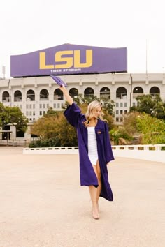 a woman in a purple graduation gown is holding her arms up