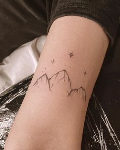 a small tattoo on the arm of a woman with mountains and stars in the sky