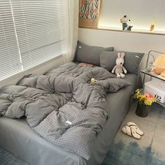 an unmade bed in the corner of a room with stuffed animals on the floor