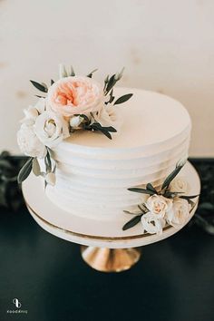 there is a white cake with flowers on the top and bottom, sitting on a gold stand