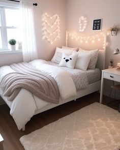 a bedroom with white bedding and string lights on the headboard, windows, and rugs