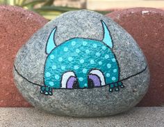 a rock painted with an image of a blue monster sitting on top of some rocks