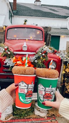 two people holding up coffee cups in front of an old red truck with christmas wreaths on it