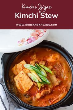 kimchi stew with tofu and vegetables in a black bowl on a white table