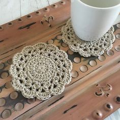 two crocheted coasters sitting on top of a wooden table next to a cup