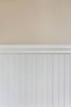 a cat sitting on top of a wooden bench in front of a white paneled wall