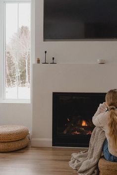 a woman sitting on the floor in front of a fire place with a television above her head