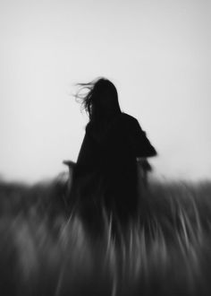 a blurry image of a woman in a field with her hair blowing in the wind