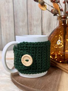 a green crocheted coffee cup cozying next to a vase with flowers