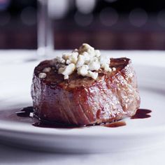 a white plate topped with meat covered in sauce and garnished with feta cheese