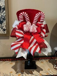 a red and white candy cane christmas bow on a black stand in front of a painting