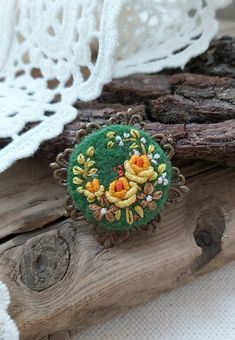 a green brooch with flowers on it sitting next to some wood pieces and lace