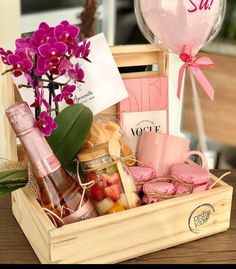 a wooden box filled with lots of pink flowers next to a wine glass and balloon