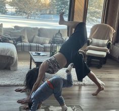 two people doing handstands on the floor in front of a living room window