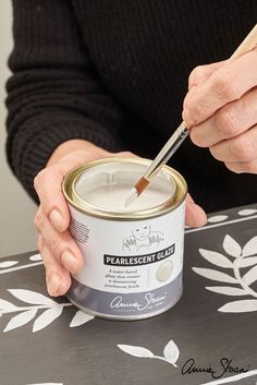 a person is holding a paintbrush and painting the inside of a can on a table