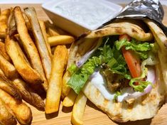 a pita sandwich and french fries on a cutting board