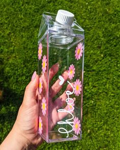 a hand holding a water bottle with pink flowers on it and the word love spelled in white letters