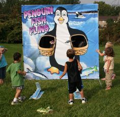 children are playing in the grass near a penguin fish ring sign that is on display