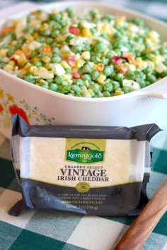 a white bowl filled with peas next to a wooden spoon and bag of vintage irish cheddar