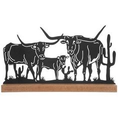 a metal cow and calf standing next to each other on a wooden base with cactus in the background