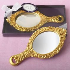 two golden mirrors sitting next to each other on a pink tableclothed surface with a white bow