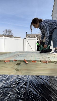 a woman in plaid shirt working on wood planks with a power drill and saw