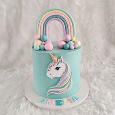 a blue cake with a unicorn head and rainbow decorations on it's top, sitting on a white furnishing