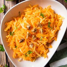 a white bowl filled with shredded carrots and nuts on top of a wooden table