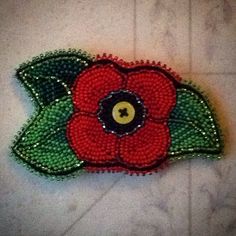 a red flower with green leaves is on the floor next to a white tile wall