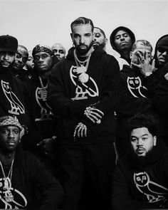 a group of men standing next to each other in front of a white wall wearing black hoodies