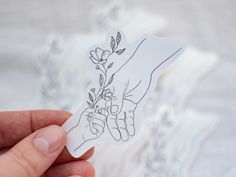 a hand holding a flower sticker in front of a white sheet with flowers on it