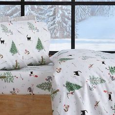 two beds covered with christmas themed sheets in front of a snowy mountain scene and window