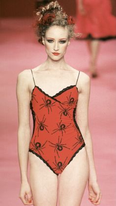 a model walks down the runway in a red and black swimsuit with spider webs on it