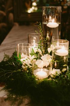 candles and greenery are arranged on the table for an elegant centerpiece with white flowers