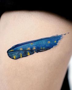 a woman's thigh with a blue and yellow feather tattoo on her left side