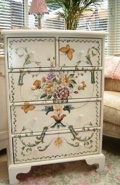 a white dresser with flowers painted on the front and drawers, sitting in a living room next to a couch