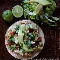 two tacos with avocado and limes on the side next to a salad