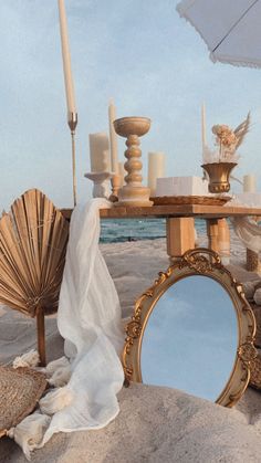 a table with an umbrella, mirror and shells on the sand at the ocean shore