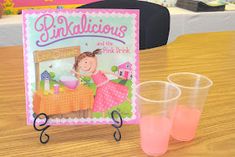 two plastic glasses sitting on top of a wooden table next to a pink book and cup