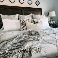 a bed with pillows and blankets on it in front of three mirrors above the headboard