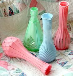 four different colored vases sitting on top of a quilted bedspread,