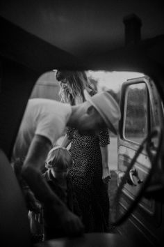 a black and white photo of people standing in front of a car with the door open