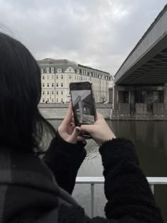 a person holding up a cell phone in front of a bridge over water with buildings on either side