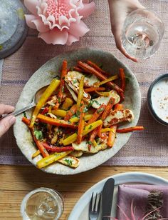 a bowl filled with carrots and other food on top of a table next to two glasses