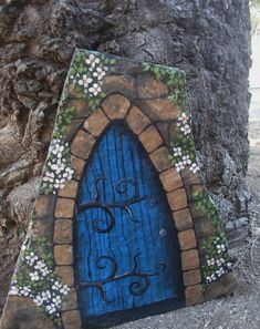 a blue door with vines and flowers painted on it's side in front of a rock wall