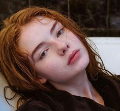 a woman with red hair laying in a bathtub