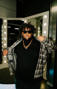 a young man wearing sunglasses standing in front of a mirror with his jacket over his shoulders