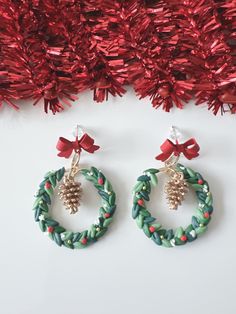 two christmas wreaths with bows and pineconis hanging from them, next to red tinsel